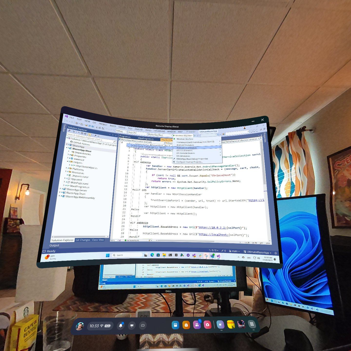 A real world office environment augmented by a virtual reality monitor. The virtual monitor shows Visual Studio with a deployment option for a Quest 3 device.