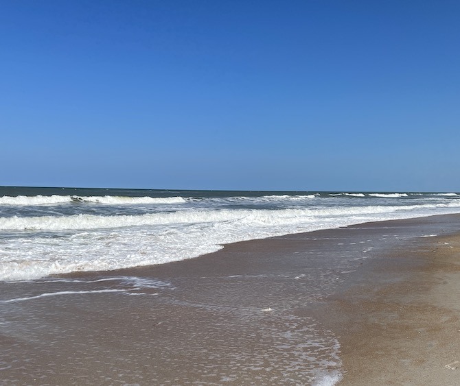 A view of St Augustine Beach in Florida. Blue skies above and the water rolling into golden brown sands below.