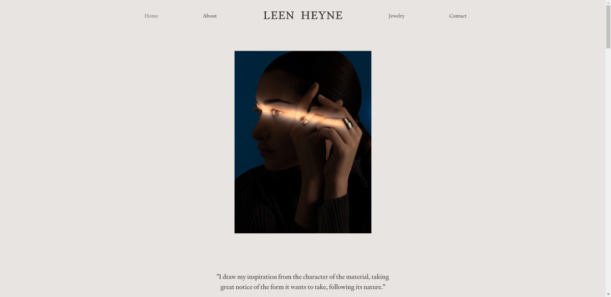 The hero section from the Leen Heyne website. Atop the oversized beige background is a dark photo of a model’s face and hands. There’s a single line of light shining through to reveal one of the jewelry artist’s rings. 